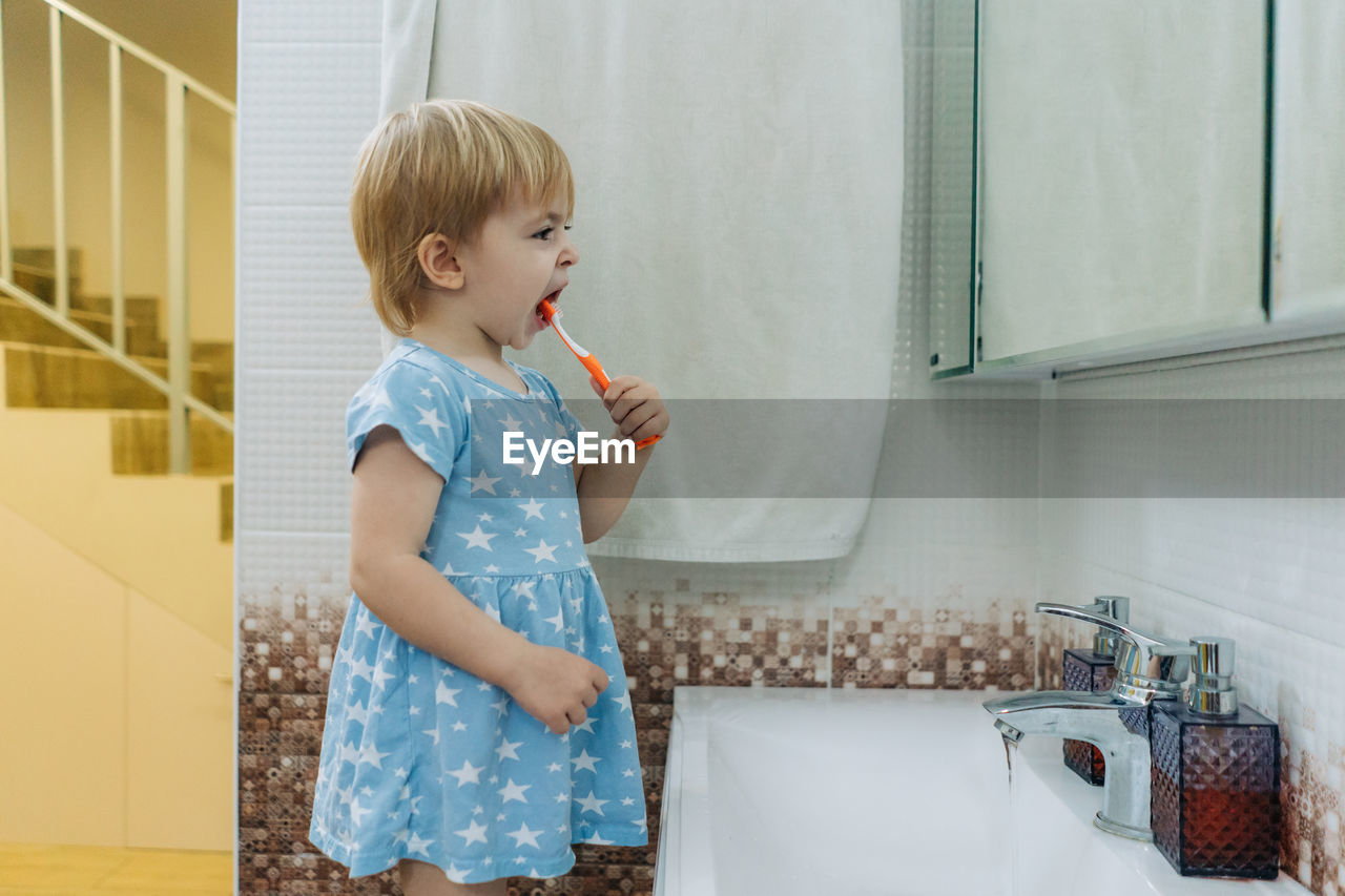 Little toddler girl brushes her teeth in the bathroom.