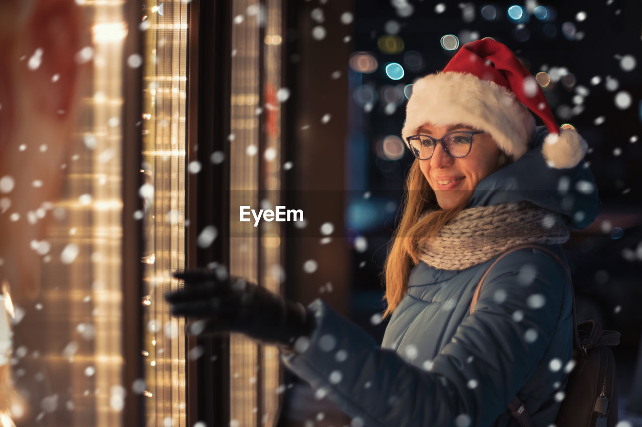 portrait of young woman standing against illuminated christmas