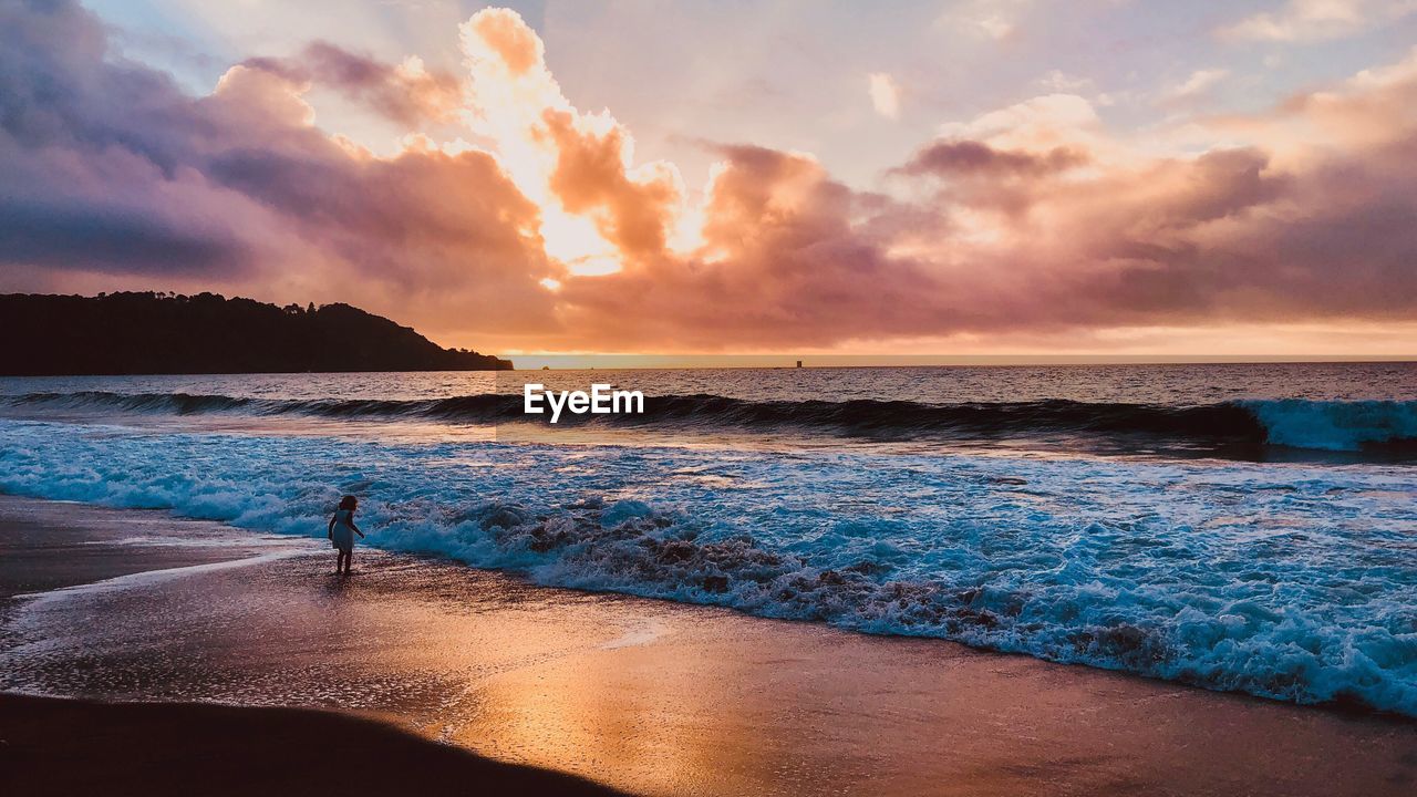 SILHOUETTE MAN STANDING ON SHORE AGAINST SKY DURING SUNSET