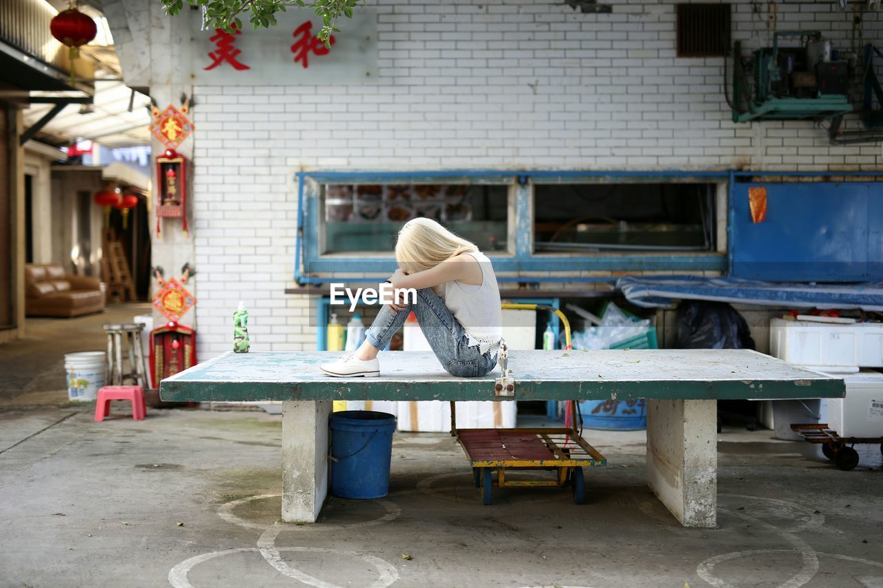 Side view of depressed woman sitting on bench at footpath