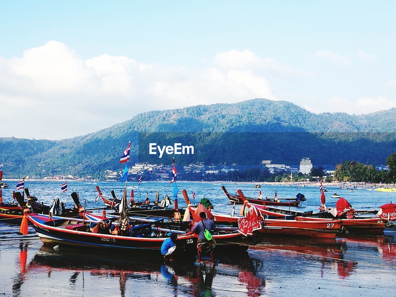 BOATS MOORED IN SEA AGAINST MOUNTAIN RANGE