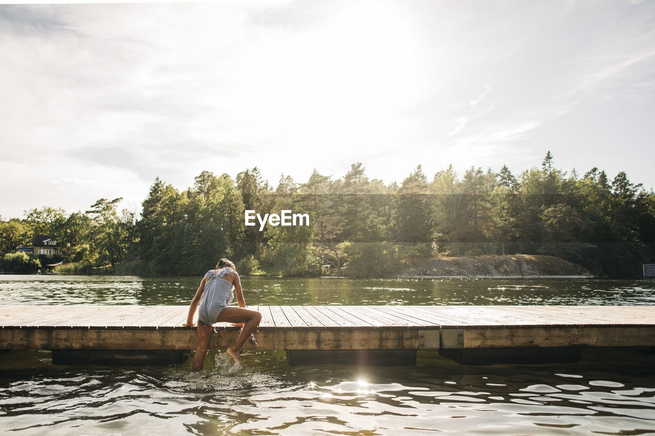 Rear view of girl climbing on jetty while coming out of lake during vacation