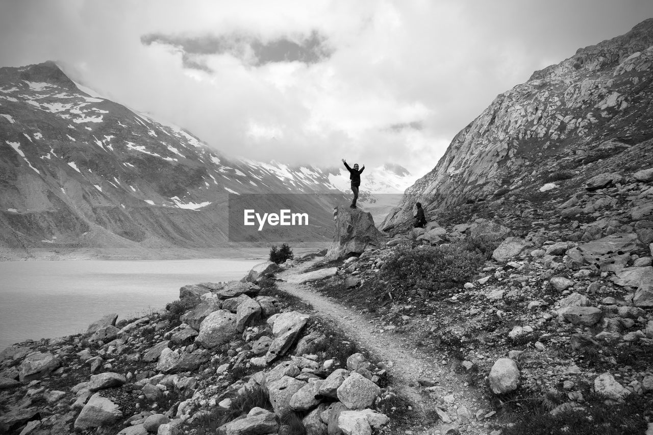 MAN ON ROCKS AGAINST MOUNTAINS