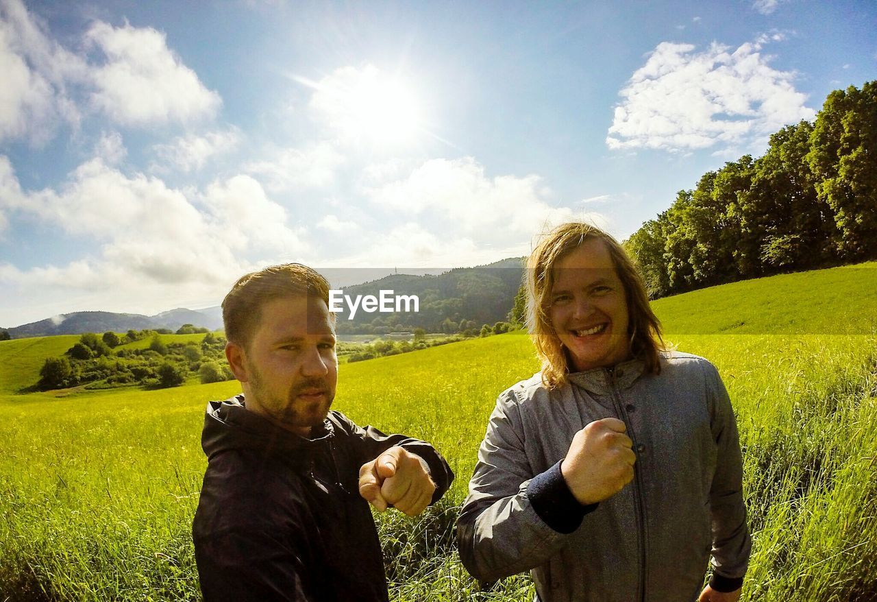 Portrait of male friends gesturing on grassy field against sky