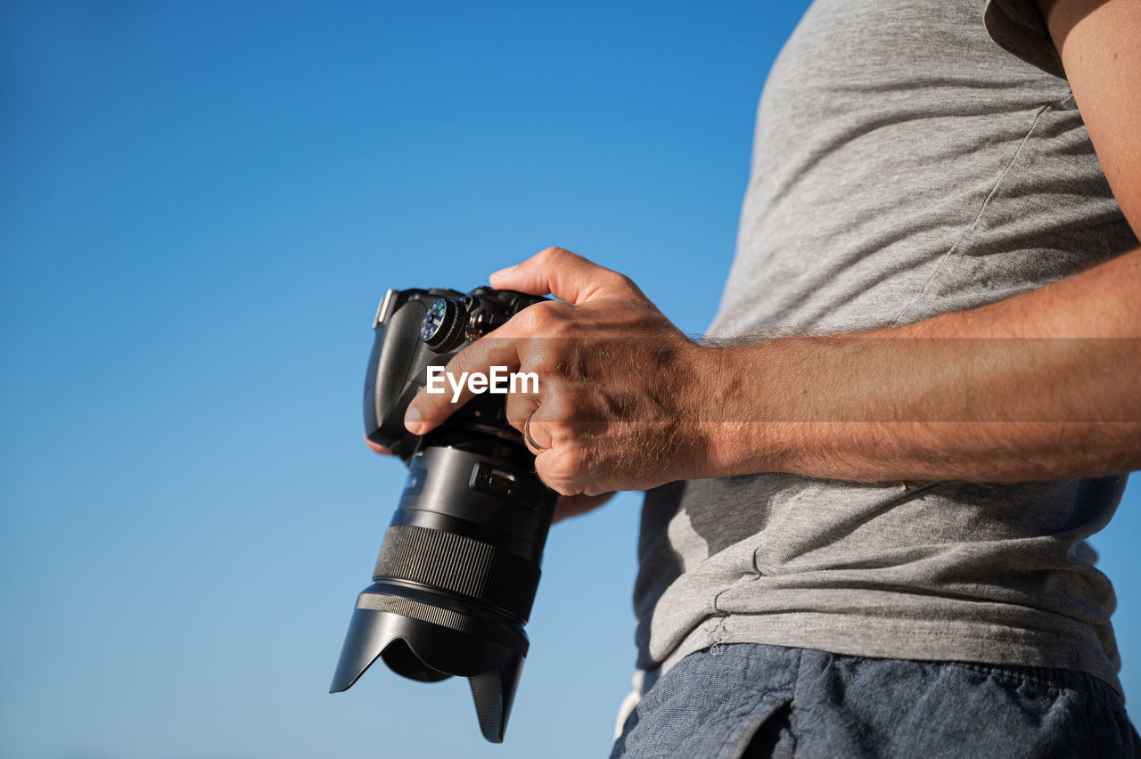 MIDSECTION OF MAN PHOTOGRAPHING AGAINST CLEAR SKY