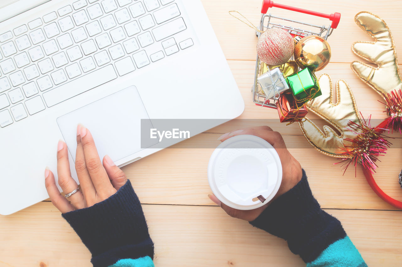 Directly above shot of hand holding coffee by laptop on table