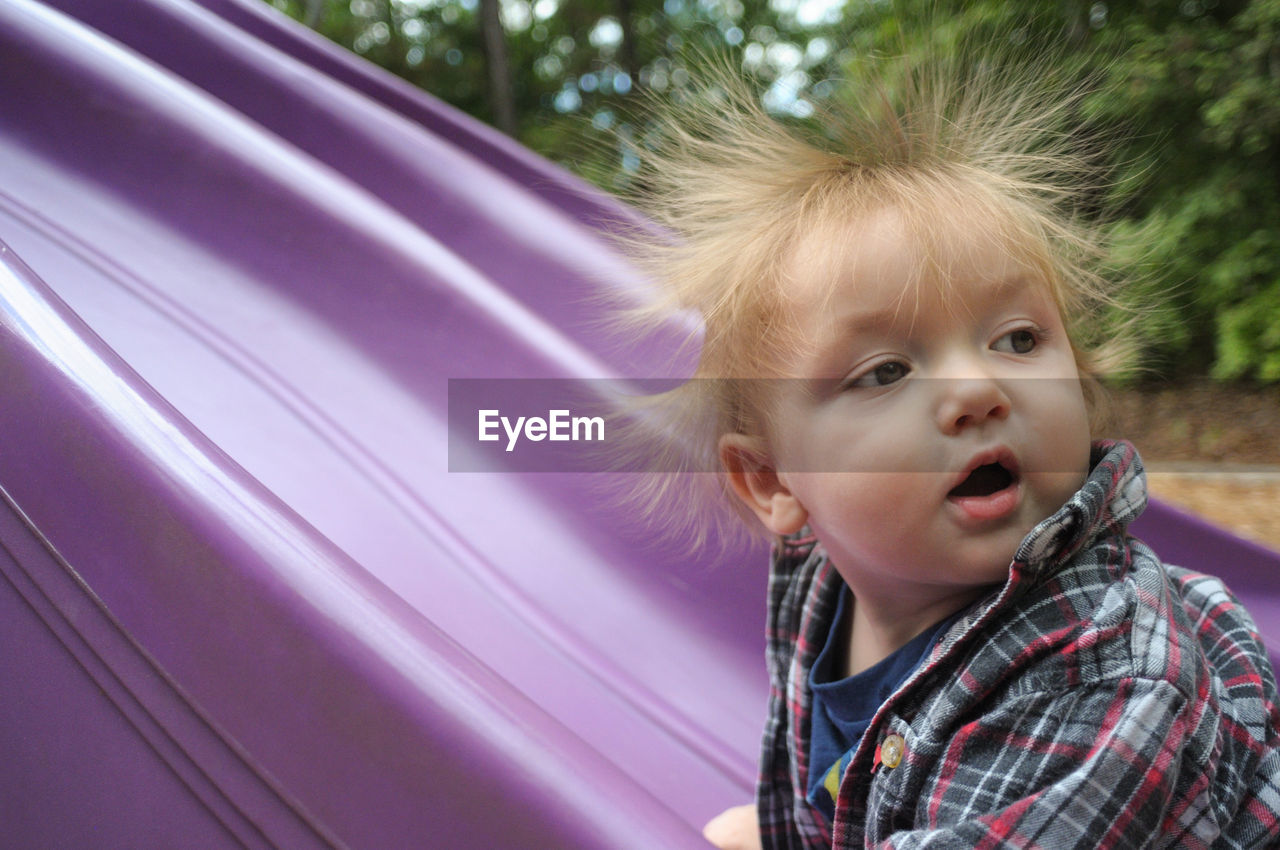 Close-up of toddler with spiked blond hair by purple slide at playground