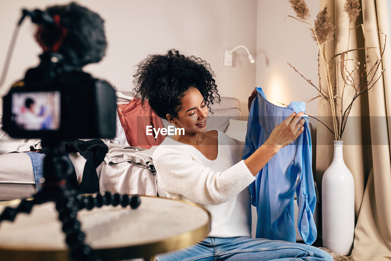 Smiling young woman looking at top with camera in foreground at home