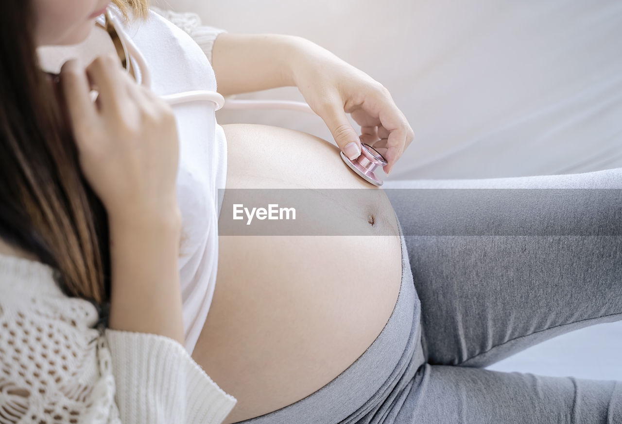 Midsection of pregnant woman holding stethoscope while sitting on sofa