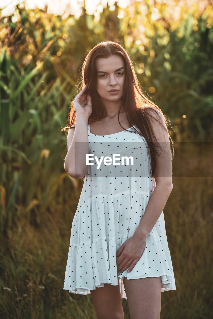 women, long hair, one person, hairstyle, young adult, adult, fashion, plant, nature, portrait, dress, standing, three quarter length, brown hair, clothing, summer, land, looking at camera, front view, smiling, teenager, child, tree, emotion, grass, sunlight, casual clothing, beauty in nature, outdoors, looking, happiness, contemplation, sunset, lifestyles, leisure activity, photo shoot, rural scene, portrait photography, relaxation, field, female, landscape, day, sky, tranquility, focus on foreground, childhood, sundress, meadow, spring, forest, serious, back lit, arts culture and entertainment, person, carefree