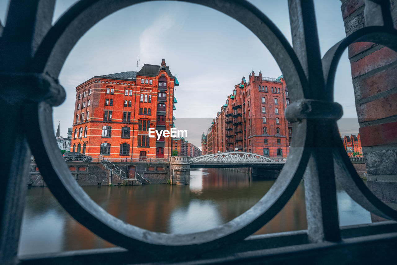 Bridge over river by buildings in city against sky