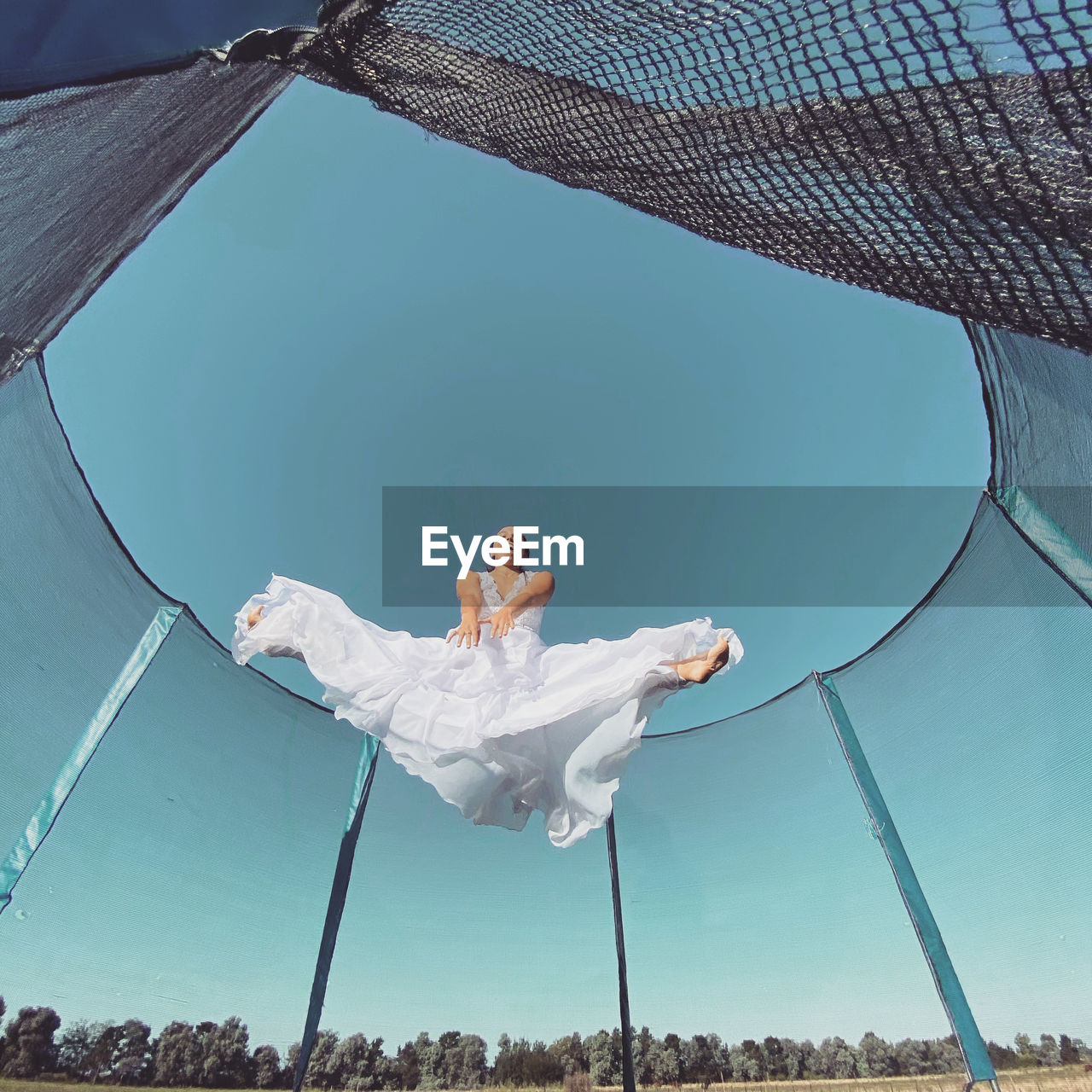 Low angle view of young woman jumping against clear blue sky