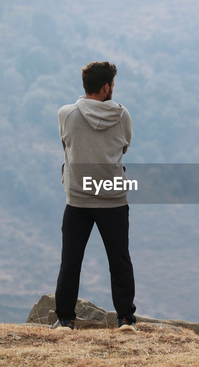 Rear view of man standing on rock against sky