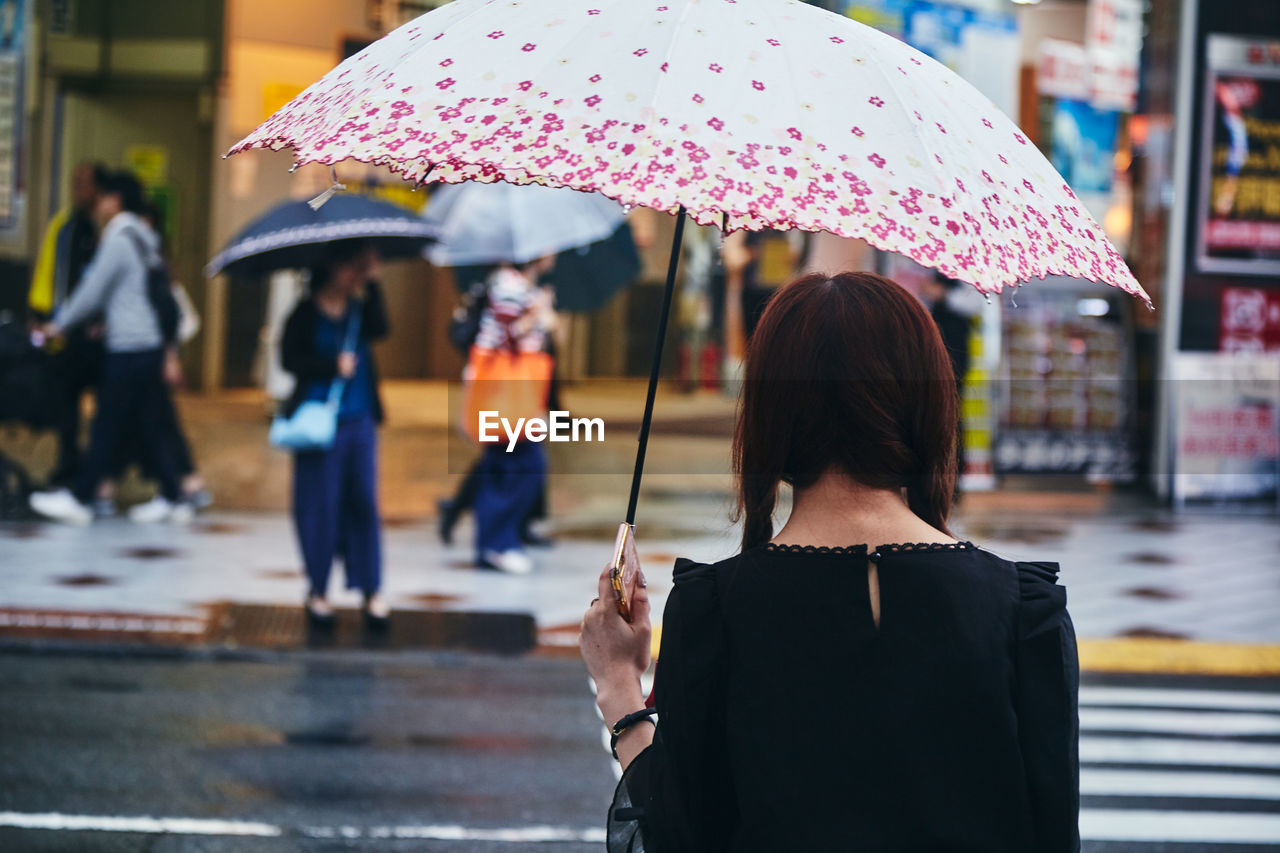 REAR VIEW OF WOMAN STANDING WITH UMBRELLA