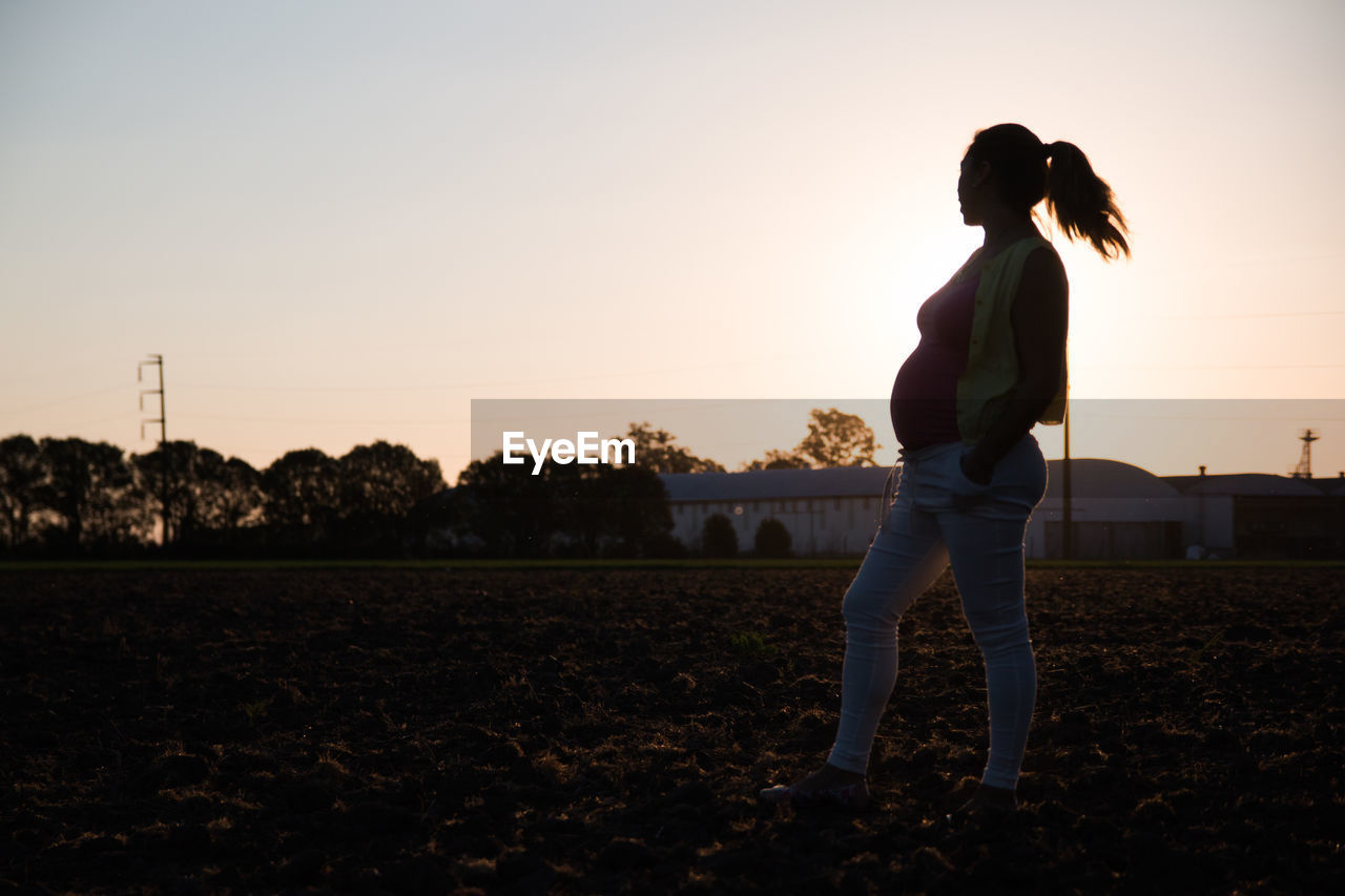 Full length of pregnant woman standing on field against sky during sunset