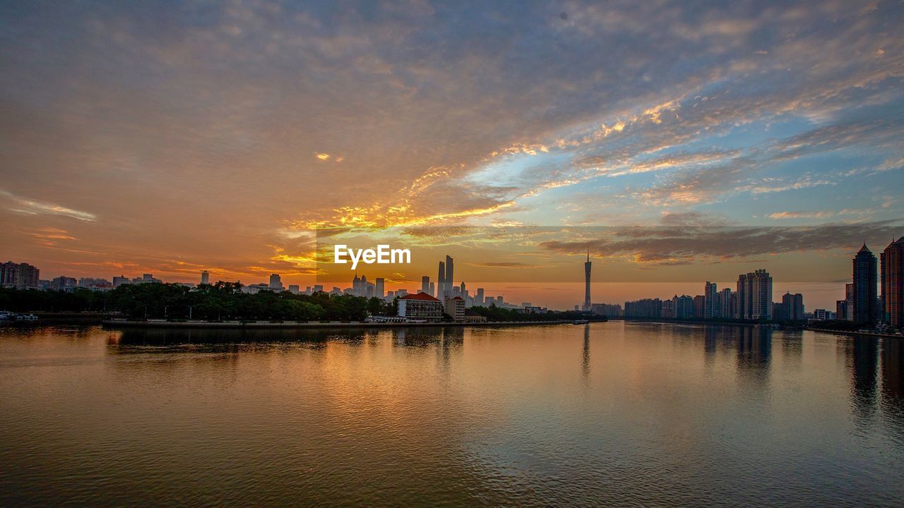 Scenic view of river by buildings against sky during sunset