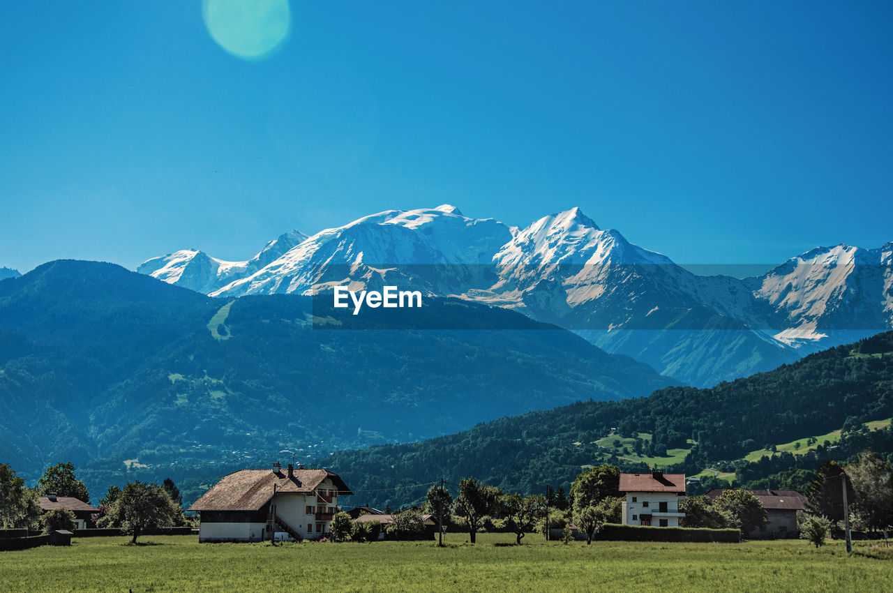 Houses by mountains against clear blue sky