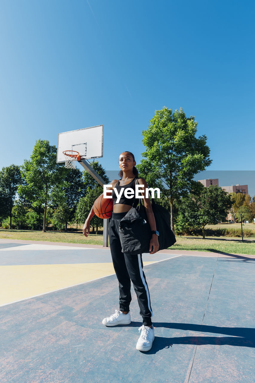 Confident sportswoman with basketball in sports court on sunny day