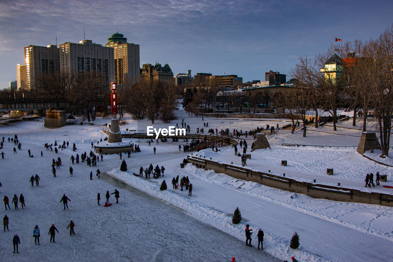 Large ice skating place, lots of people and buildings in the background
