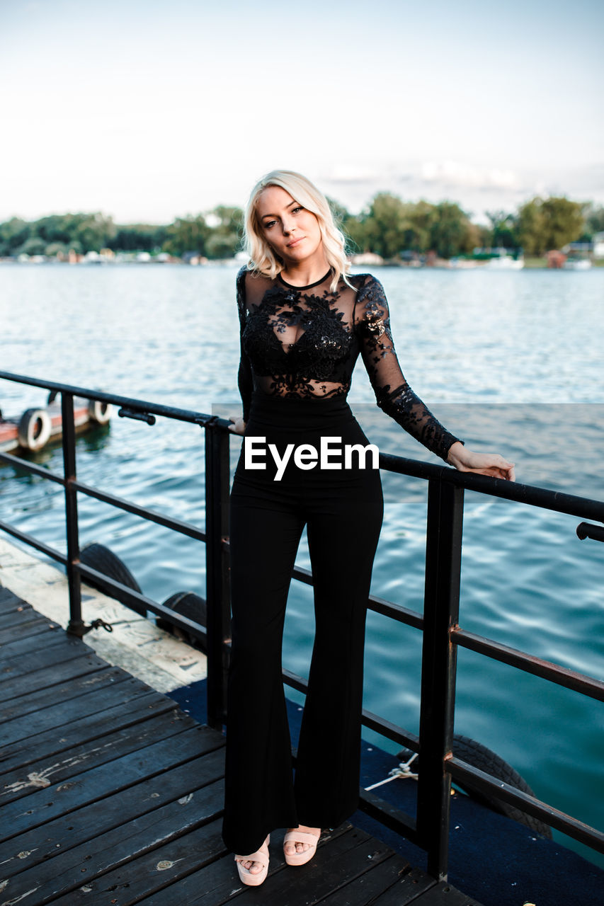 PORTRAIT OF WOMAN STANDING AGAINST RAILING IN WATER