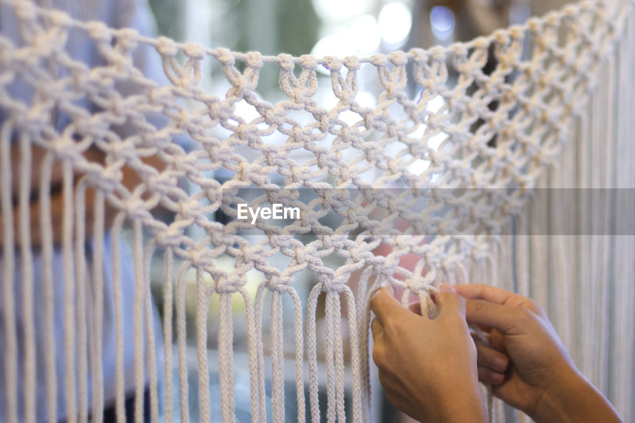 Cropped hands of woman making design with white strings