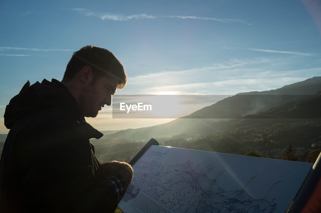 Man looking at map on mountain peak against sky during sunset