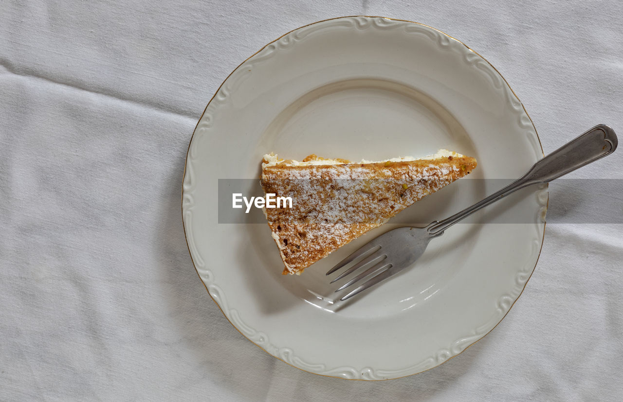 A slice of cake on a white plate with a small fork.