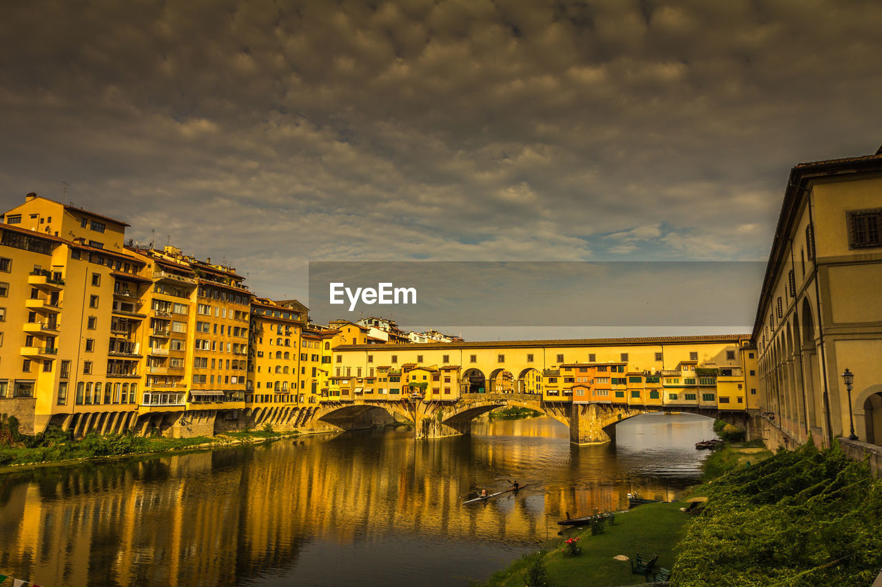 Arch bridge over river amidst buildings against sky