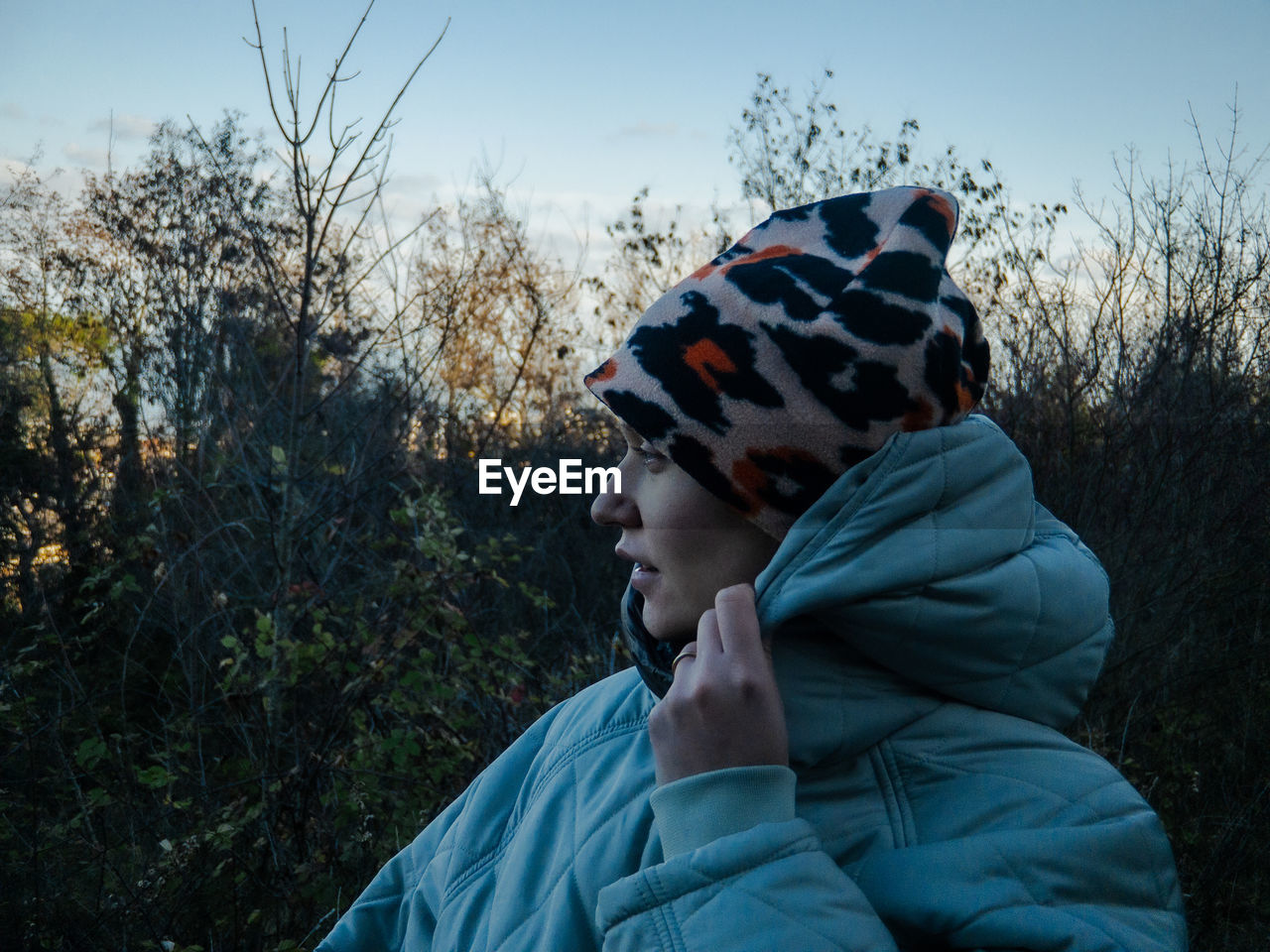 Smiling woman looking away while standing against trees during sunset