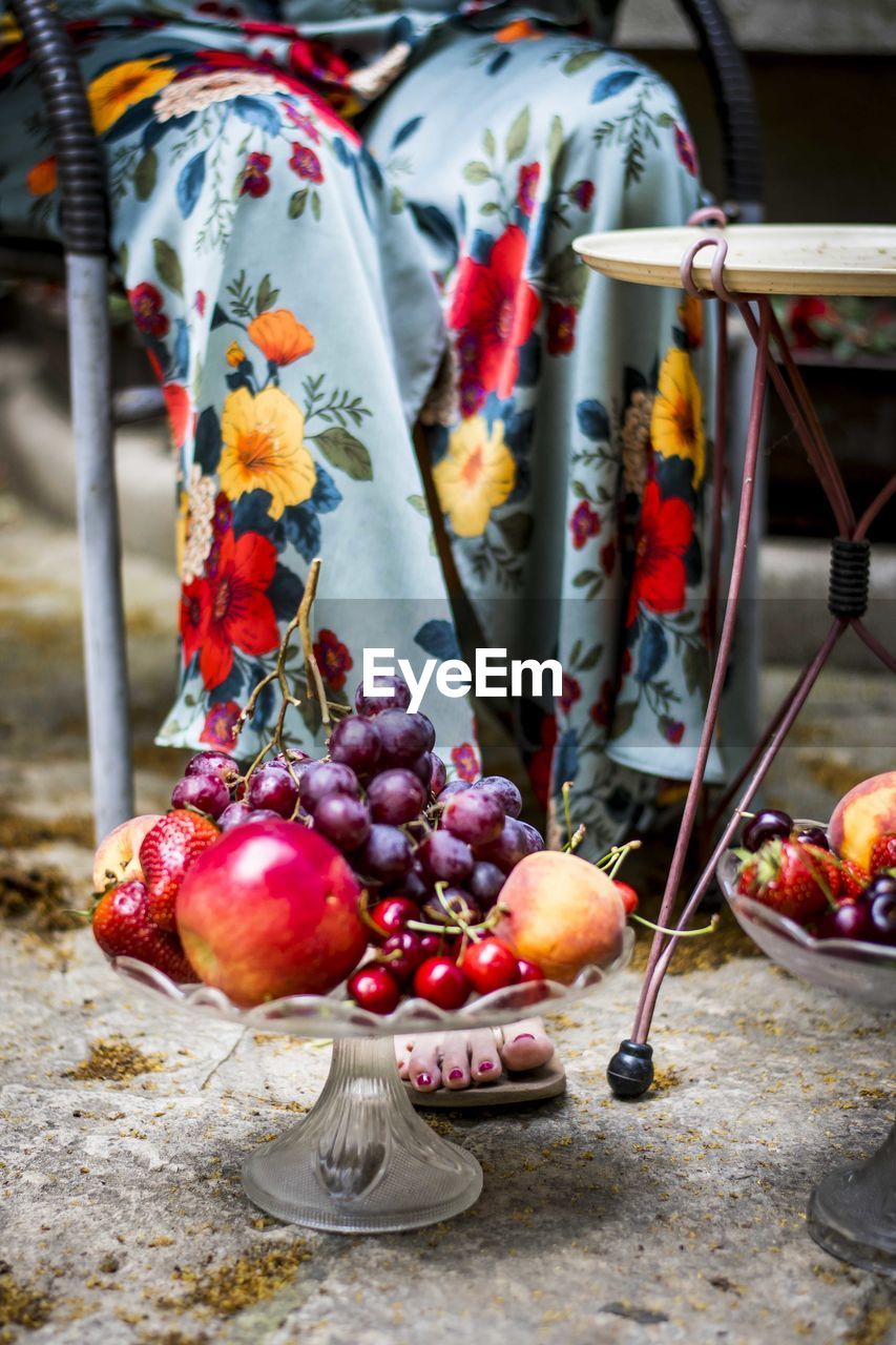 Close-up of apples and grapes in front of a woman in a floral dress