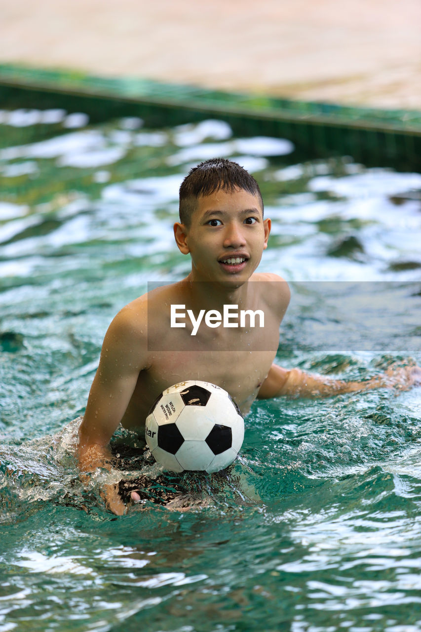 Portrait of shirtless man with ball in swimming pool