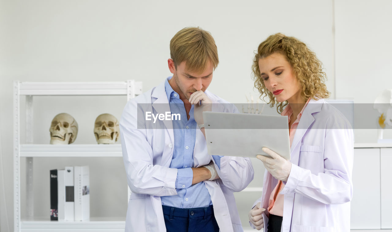 Young blonde scientist and her assistant looking at research results on the clipboard. 