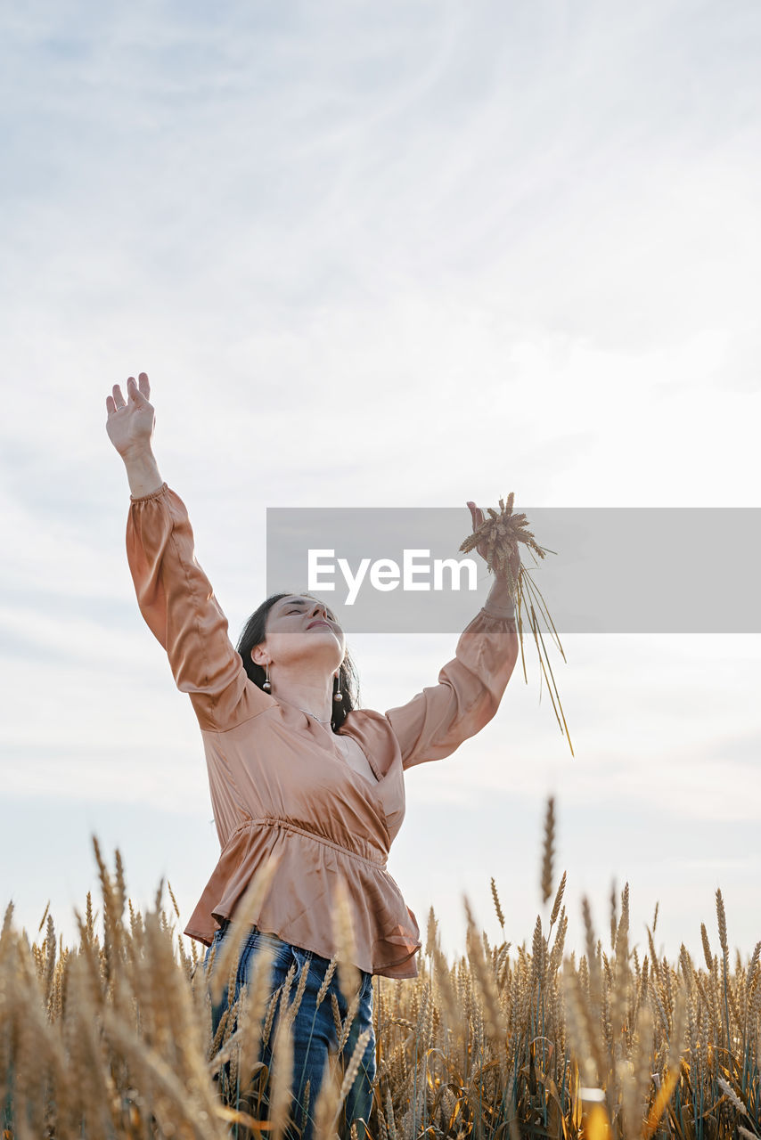 Rear view of woman with arms raised standing against sky