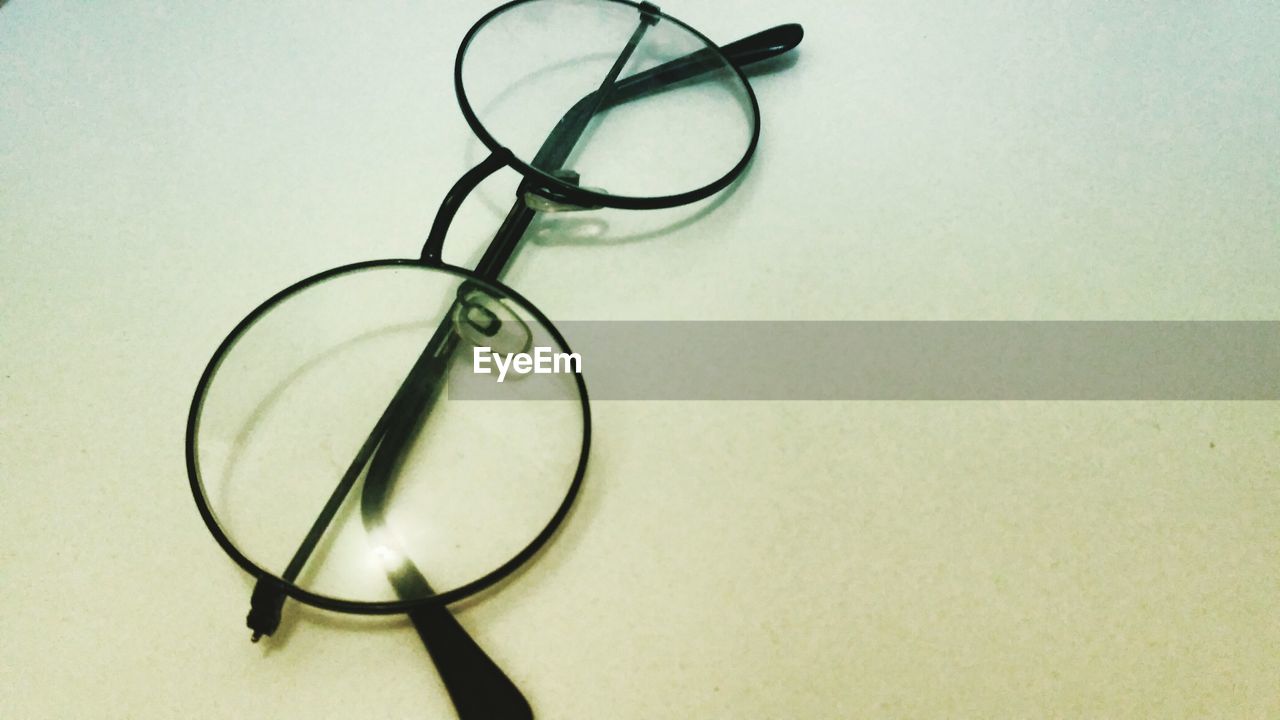 CLOSE-UP OF EYEGLASSES ON TABLE AGAINST WHITE BACKGROUND