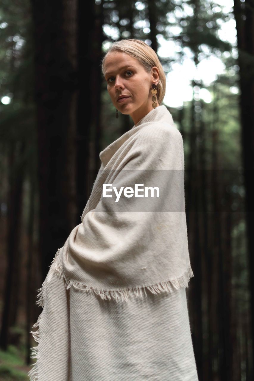 Young woman standing against trees in forest