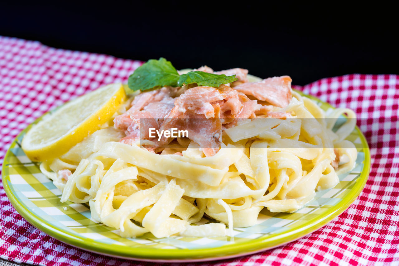Close-up of tagliatelle with salmon on table against black background