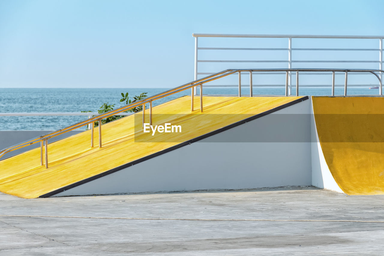 Detail of the yellow ramp skating park with blue sky and grey concerete. 