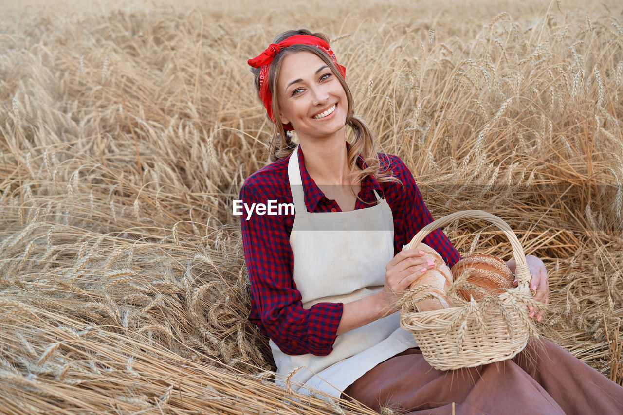 Portrait of smiling woman holding food in basket sitting on plants