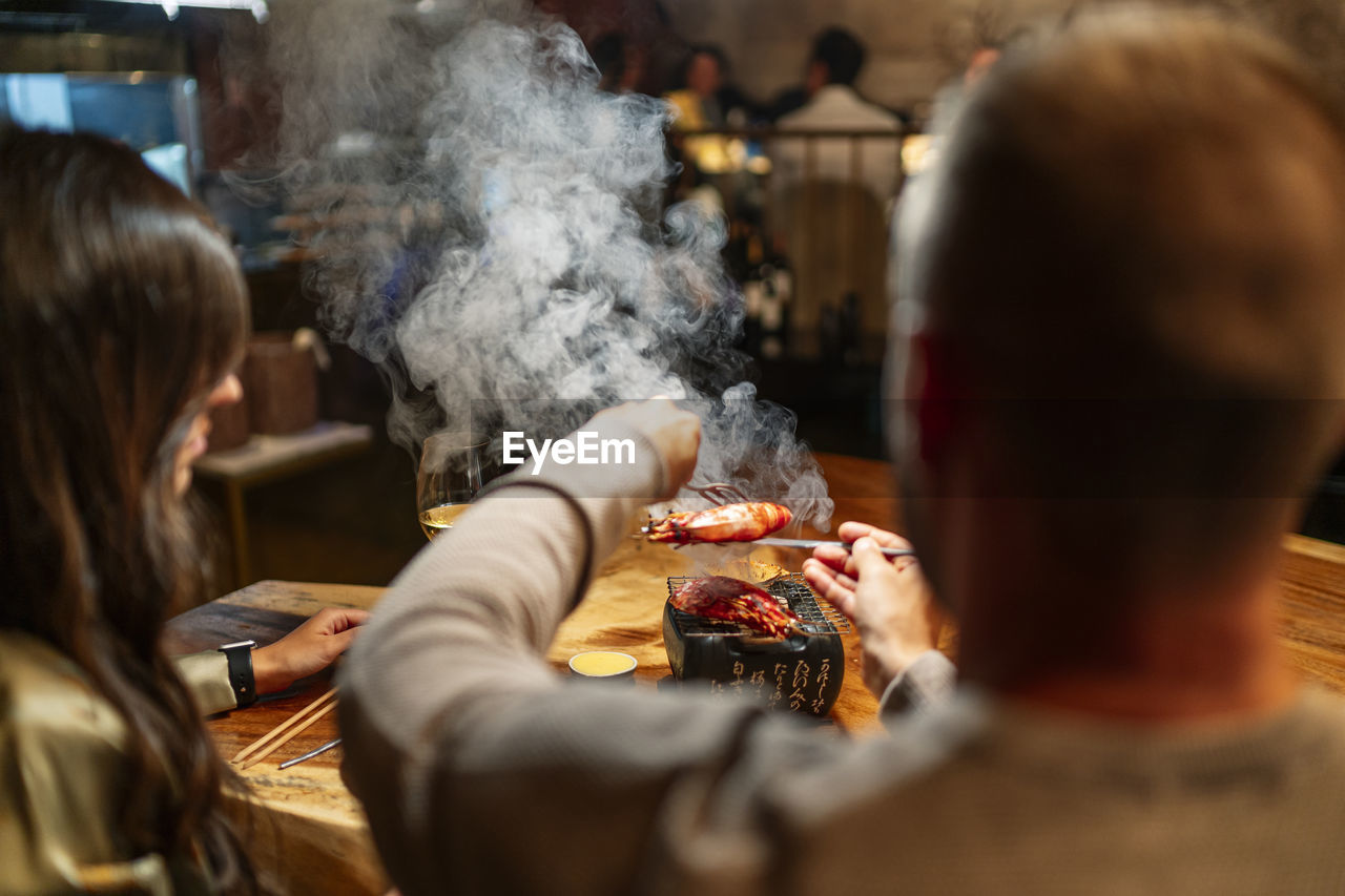 Man holding food while sitting by table at restaurant