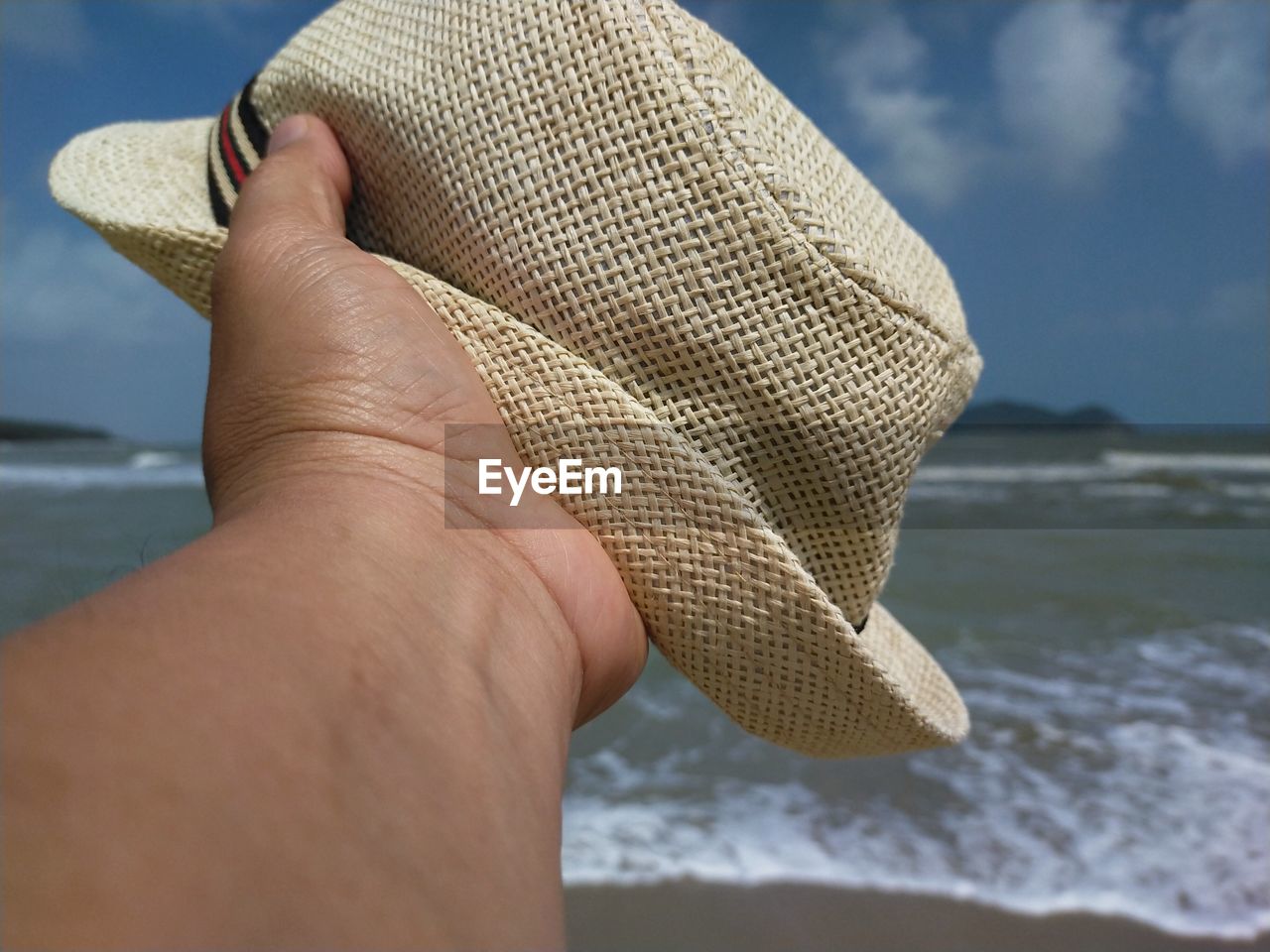 Close-up of hand holding hat against sea