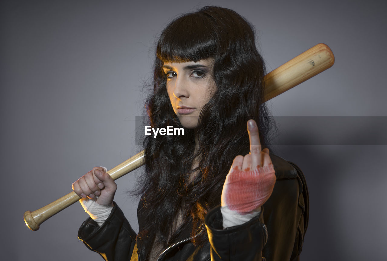 Portrait of young female model holding baseball bat against gray background