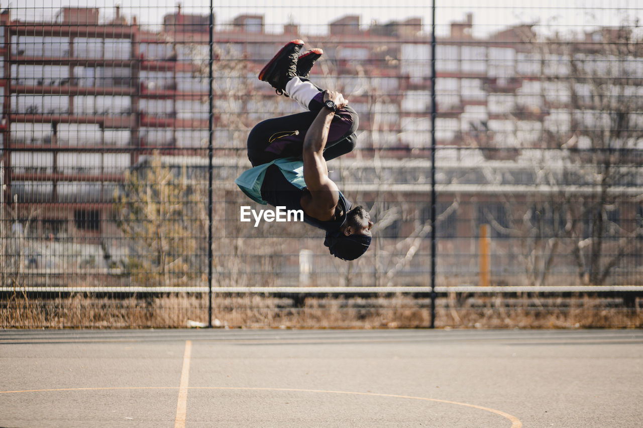 Young man practicing acrobats on sports court during sunny day