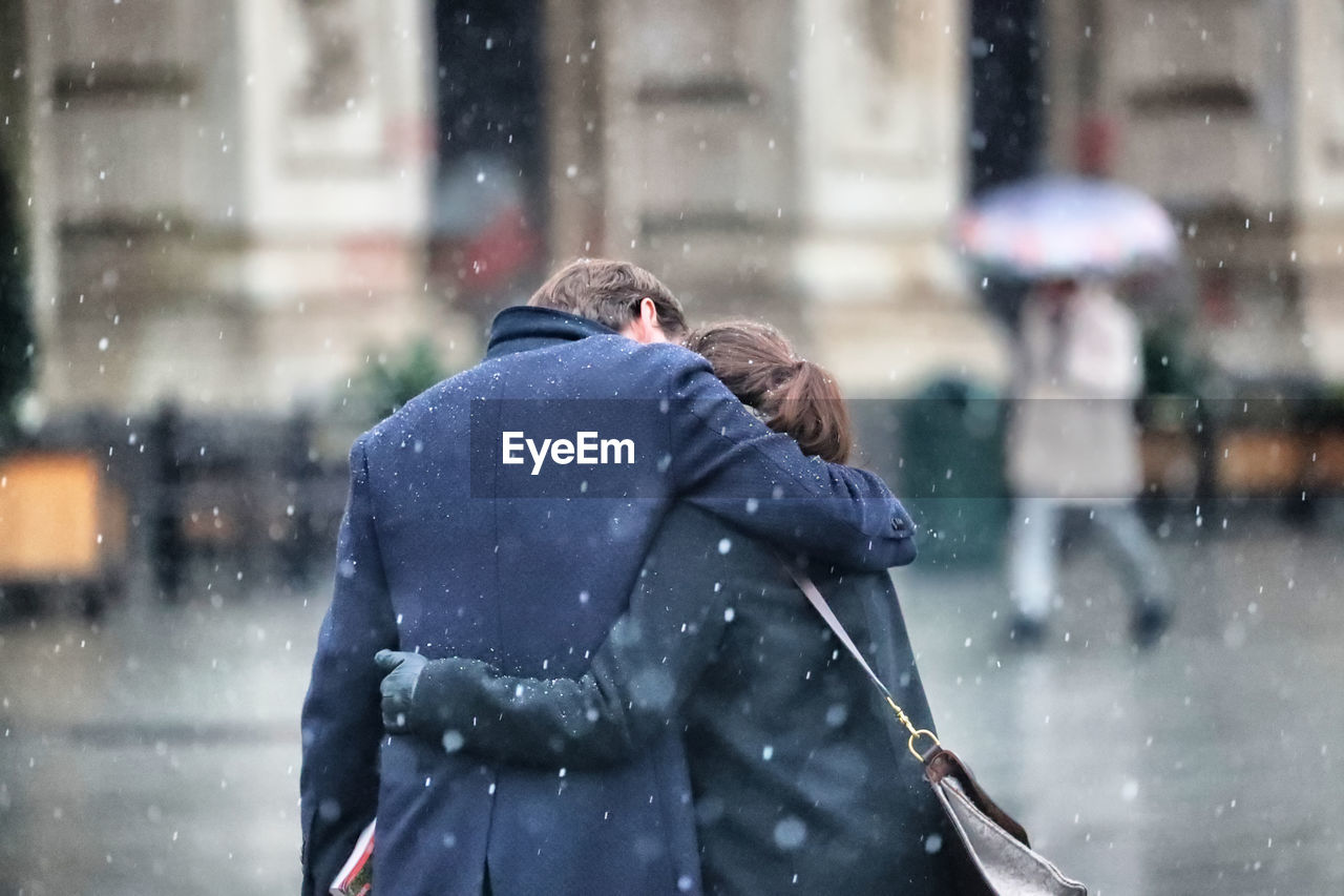 Rear view of couple embracing in city during snowfall