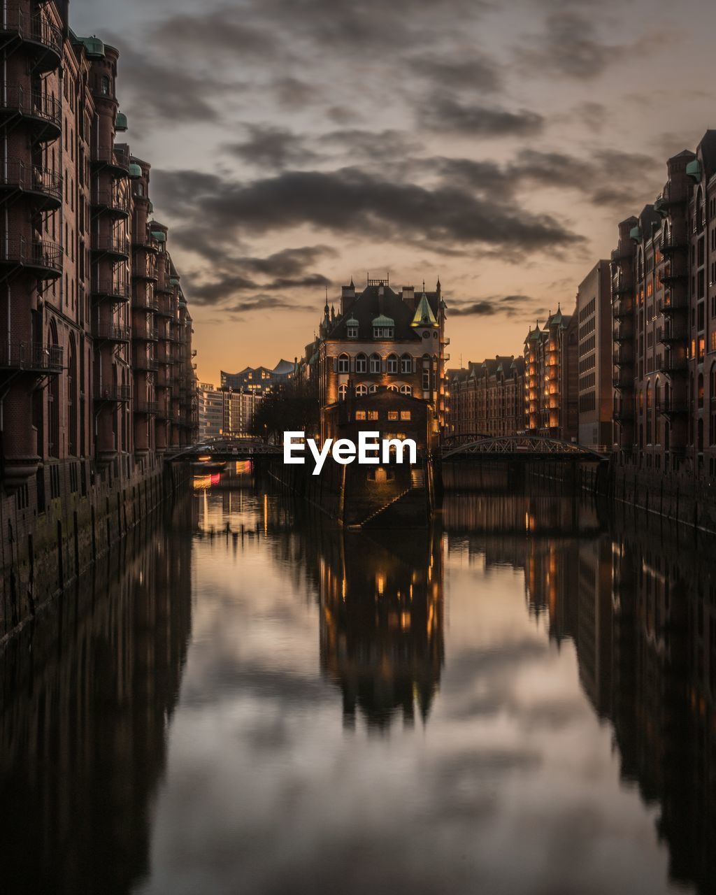 Reflection of illuminated buildings in canal against sky