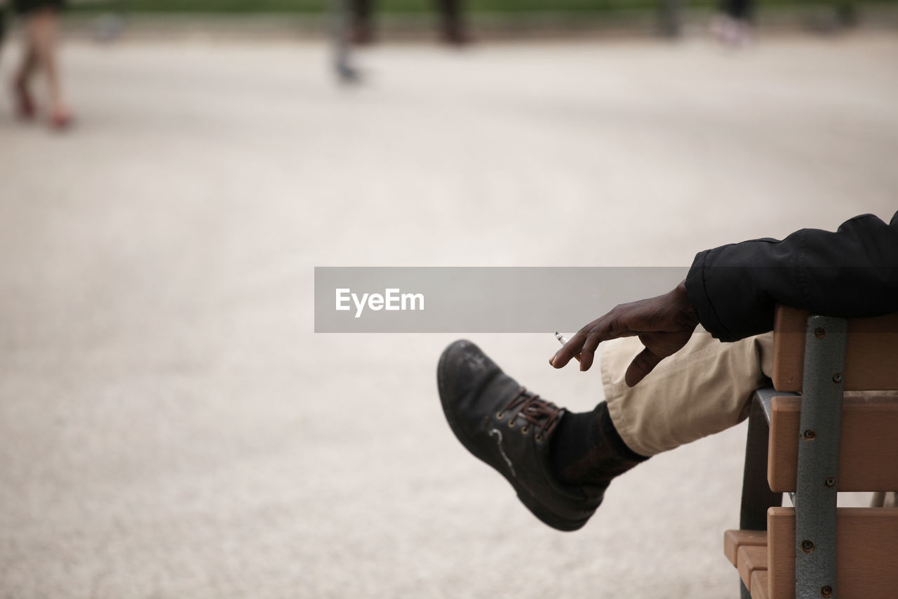 Cropped image of man holding cigarette while sitting on bench