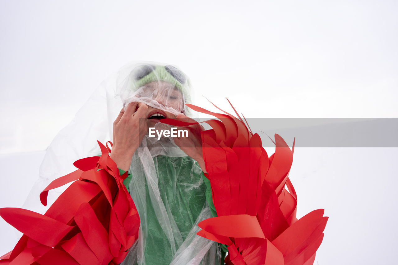 Woman wearing bird costume trying to move out from plastic against sky