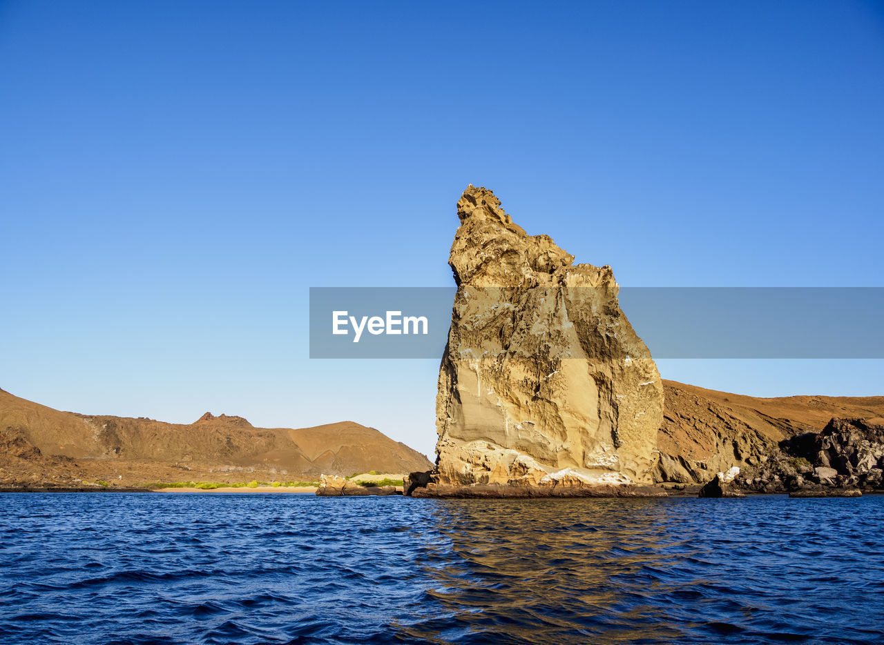 Rock formation in sea against clear blue sky