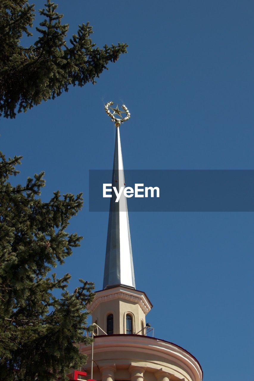 architecture, sky, tree, blue, built structure, clear sky, plant, steeple, building exterior, nature, low angle view, no people, travel destinations, tower, landmark, city, building, travel, day, sunny, spire, outdoors, religion, place of worship, the past, history, tourism, belief