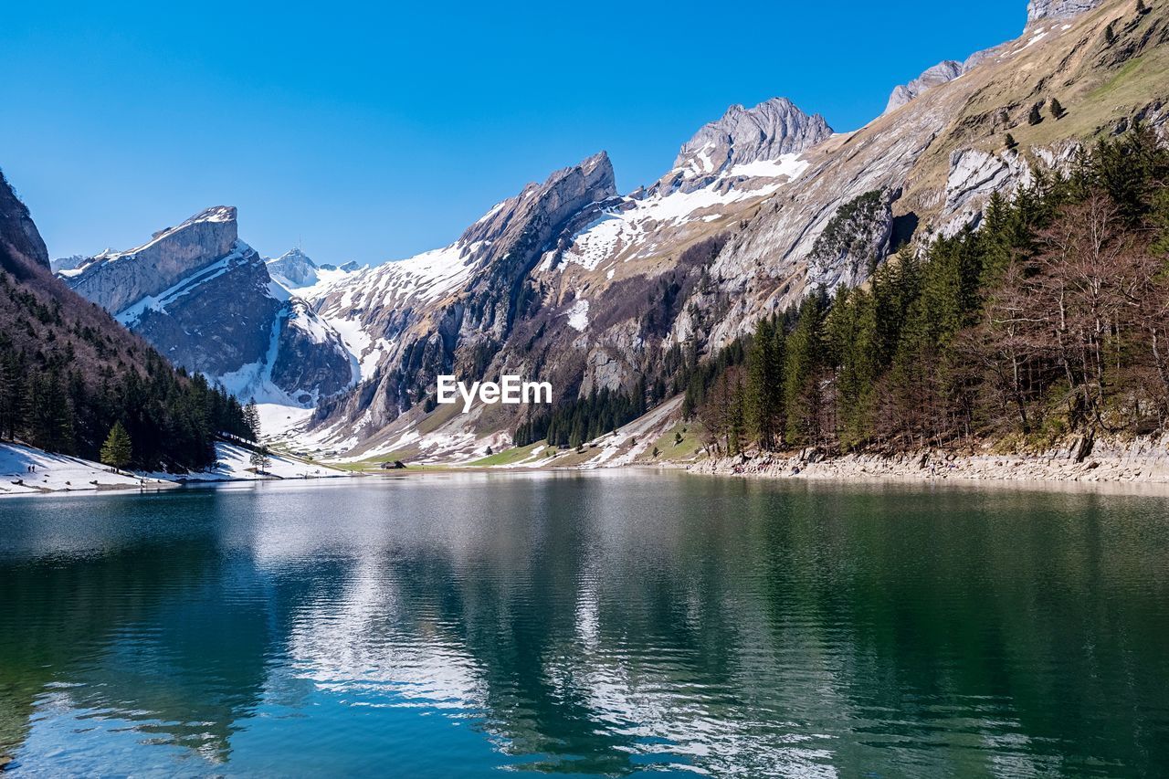 Scenic view of lake and snowcapped mountains against blue sky