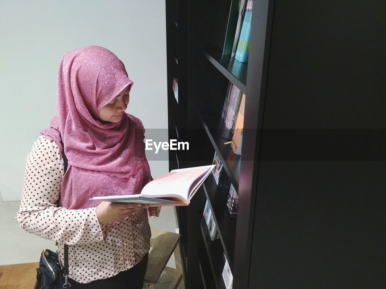 Woman reading book by bookshelf at library